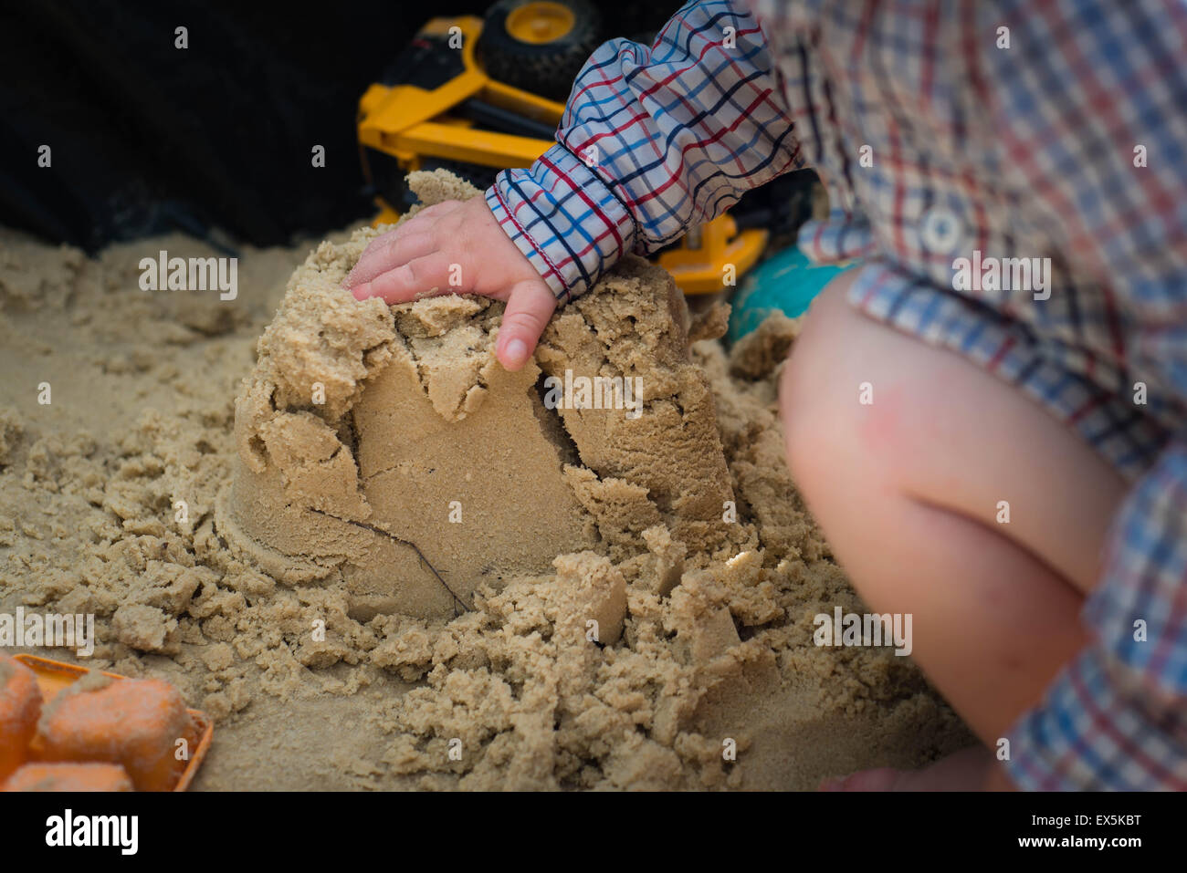 child patting sand castle with hand Stock Photo