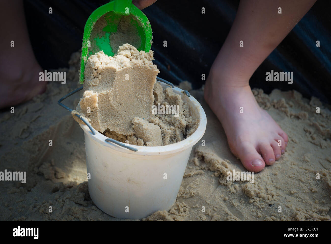 child filling bucket with sand in sand pit Stock Photo