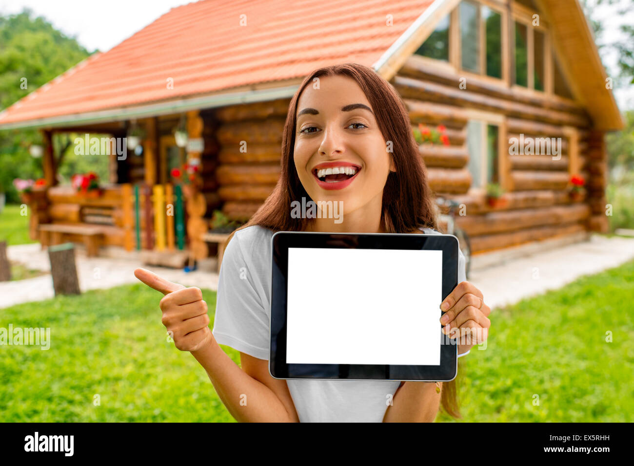 Woman showing digital tablet near the wooden cottage. Stock Photo