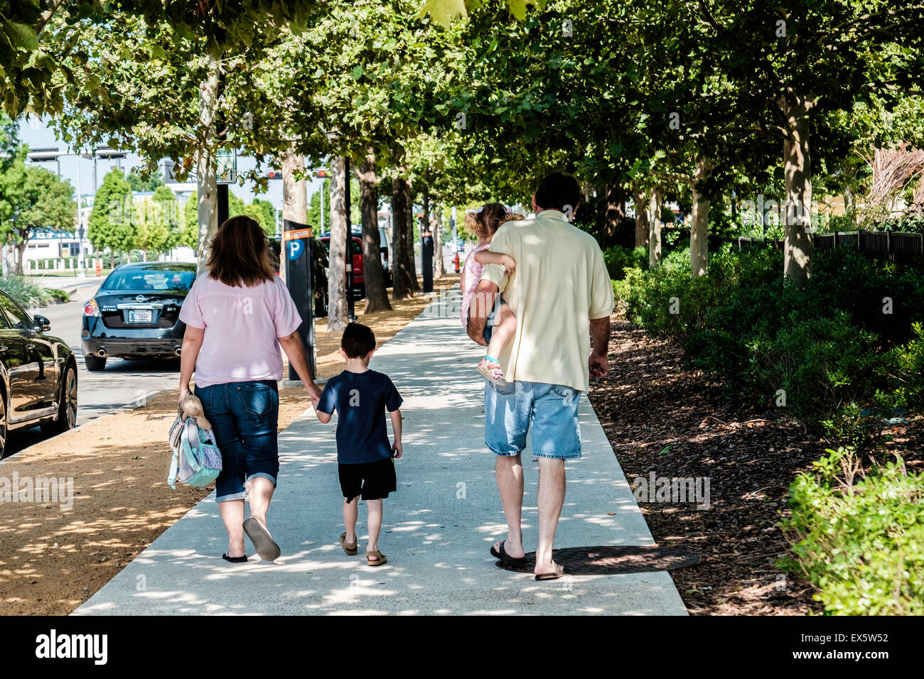 Two parents walk down a sidewalk with their two small children, a boy and a girl. Stock Photo