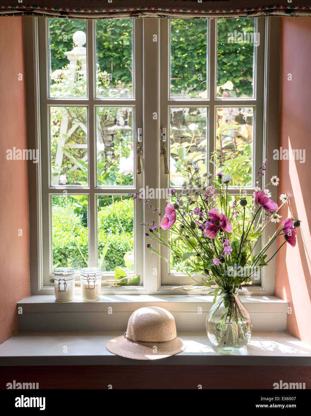 poppies and apiaceae in glass jug on windowsill with sun hat Stock Photo
