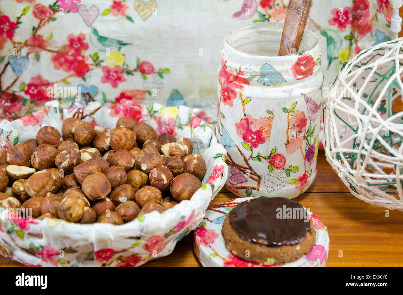 Hazelnuts in a decoupage decorated bowl on a table surrounded by decoupage decorated kitchen dishes on a wooden table Stock Photo