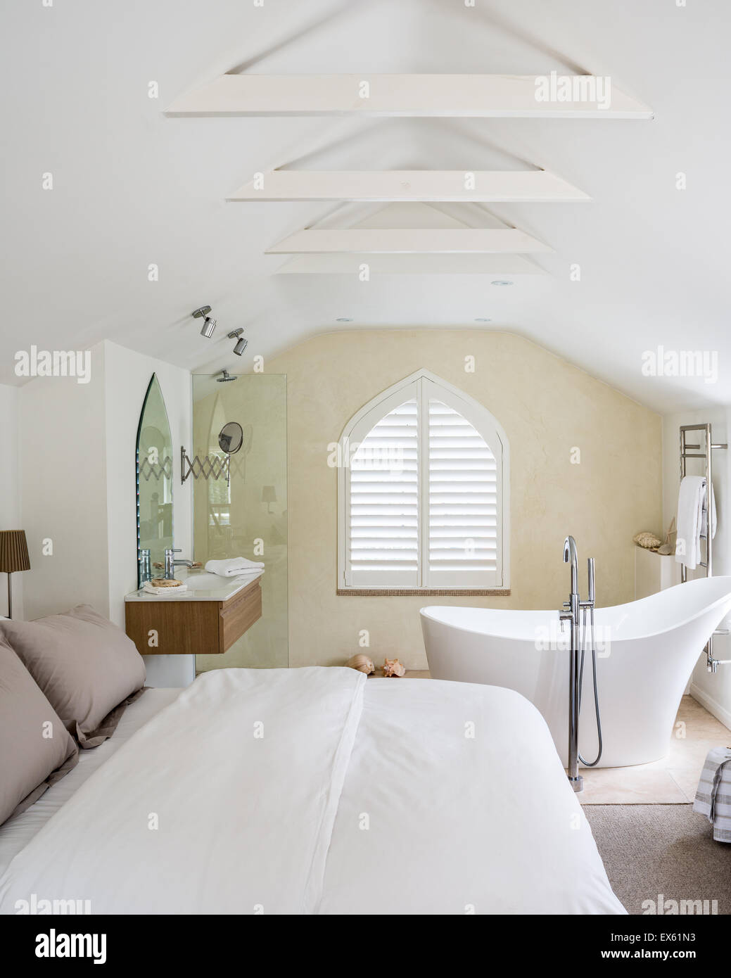 Loft style bedroom with beamed ceiling and gothic window. The limestone bath is from Victoria & Albert Stock Photo
