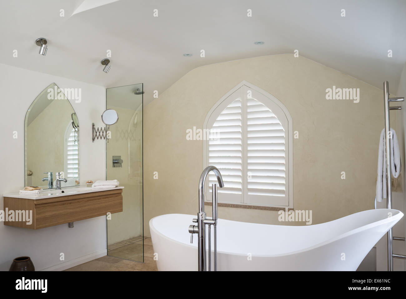 Loft style bedroom / bathroom with beamed ceiling and gothic window. The limestone bath is from Victoria & Albert and the taps b Stock Photo