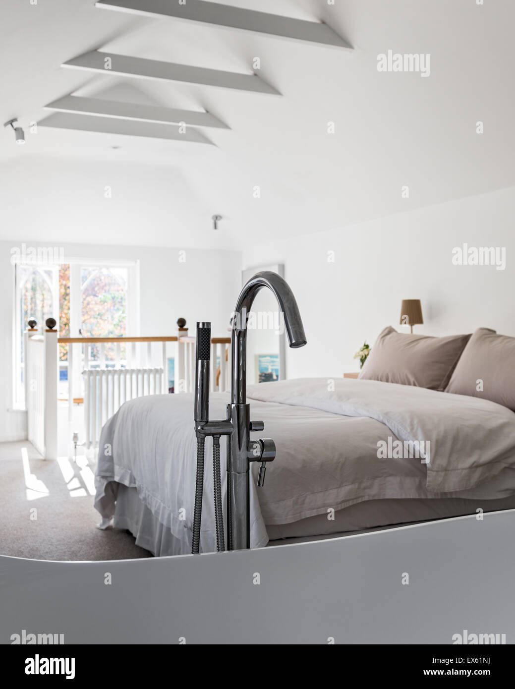 Loft style bedroom with beamed ceiling and gothic window. The limestone bath is from Victoria & Albert and the taps basin and sh Stock Photo