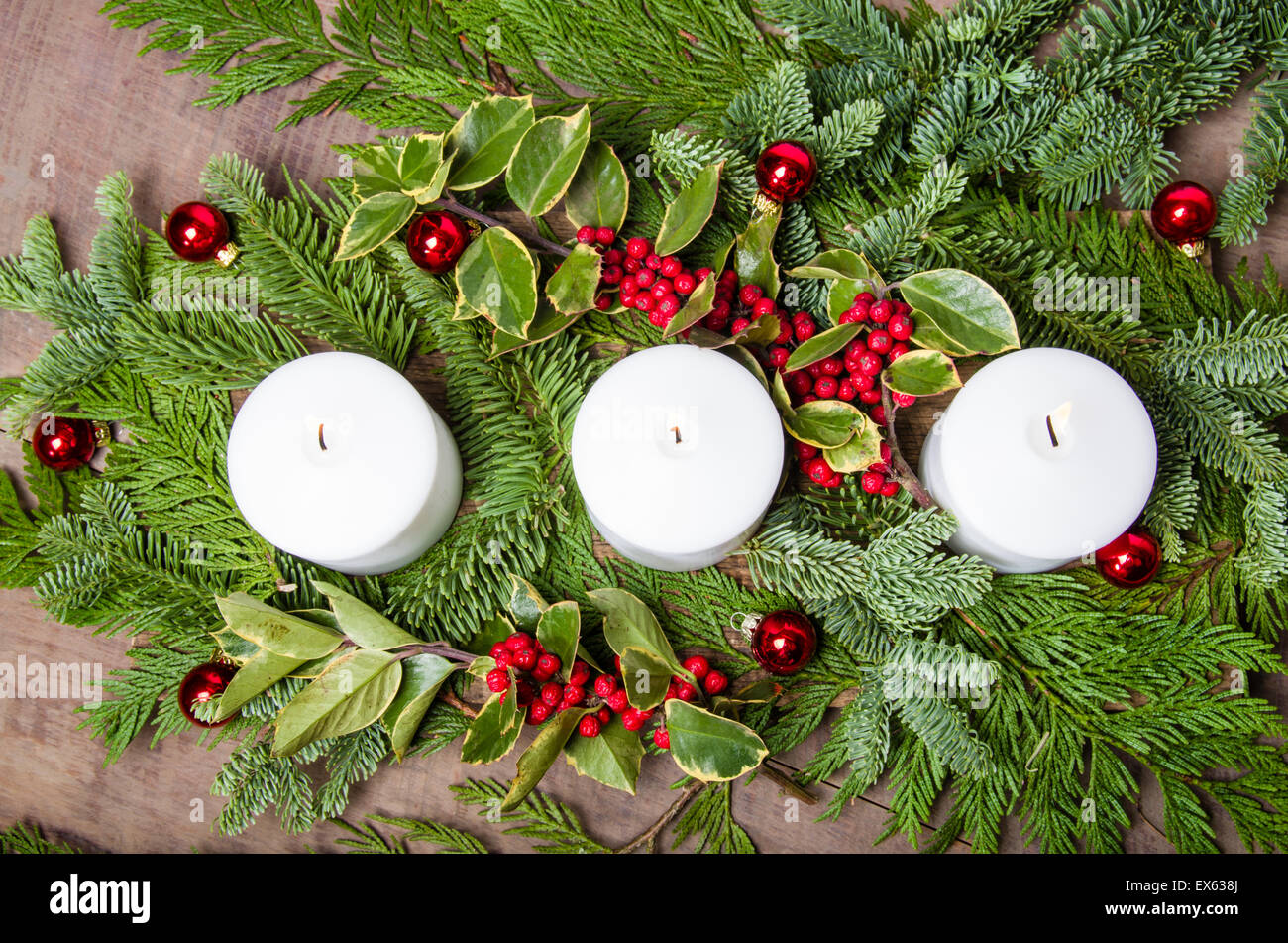 An evergreen Christmas centerpiece with three white candles and holly berries Stock Photo