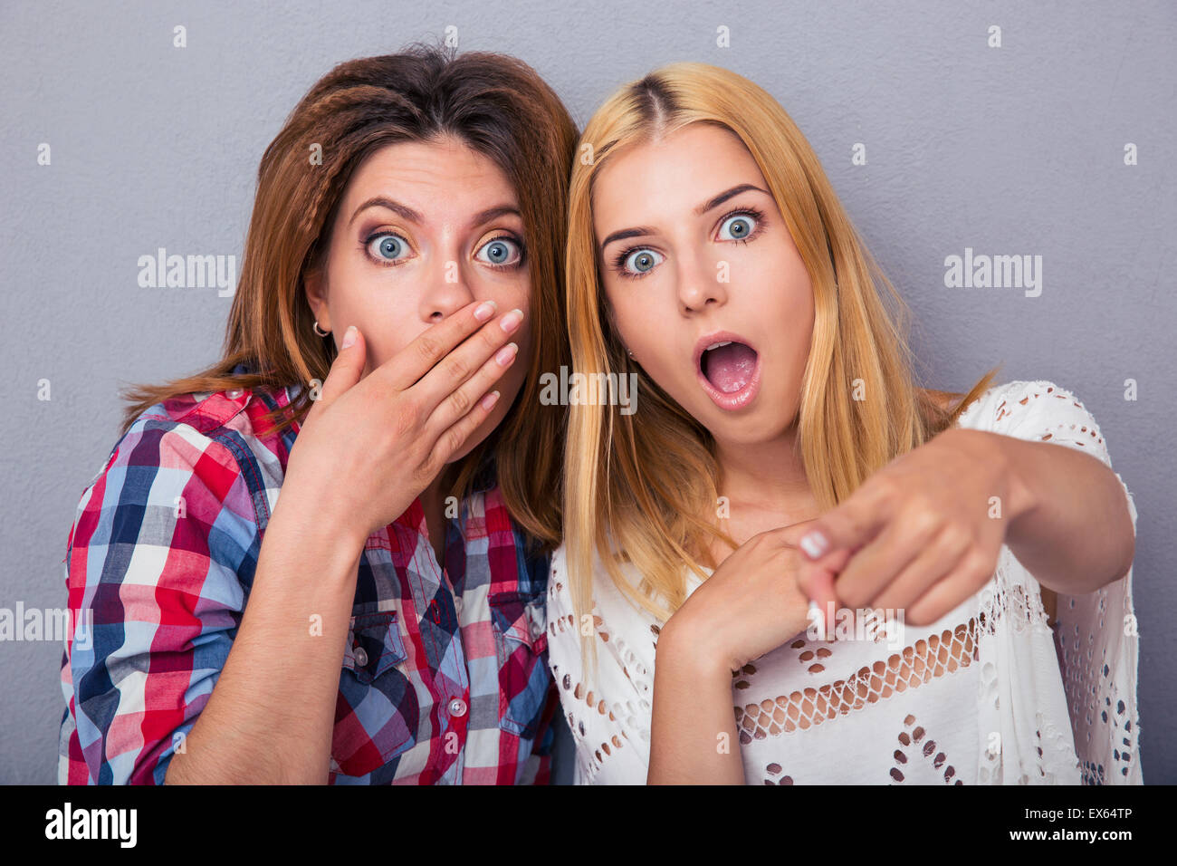 Portrait of a two surprised women standing over gray background and looking at camera Stock Photo