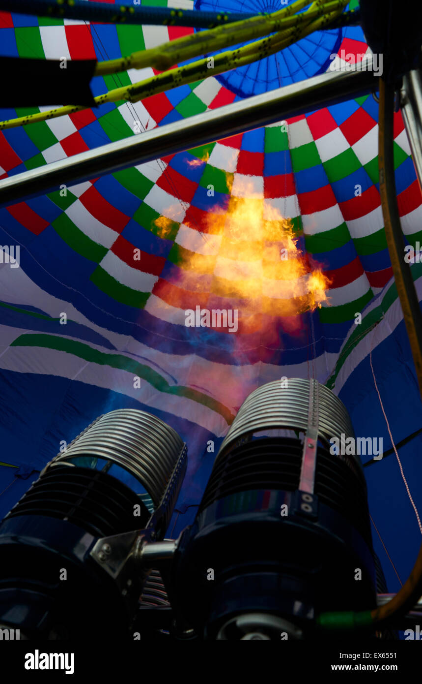 A burner with its super hot flame light up the inside of a colorful hot air balloon as it is inflated for flight Stock Photo