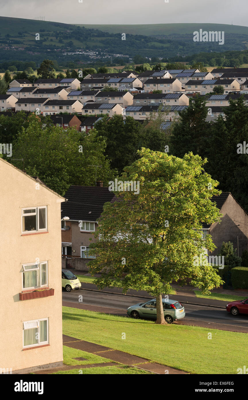 Sunlit housing with solar panelling on the roofs in the Bettws area of Newport City, Wales, Cwmbran can be seen in the distance. Stock Photo