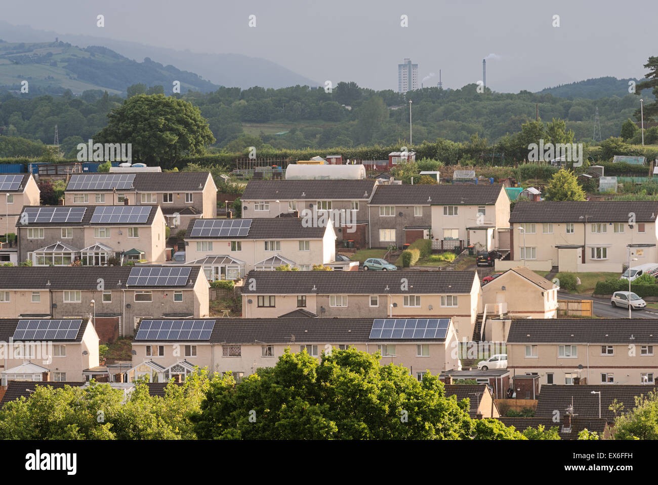 Sunlit housing with solar panelling on the roofs in the Bettws area of Newport City, Wales, Cwmbran can be seen in the distance. Stock Photo