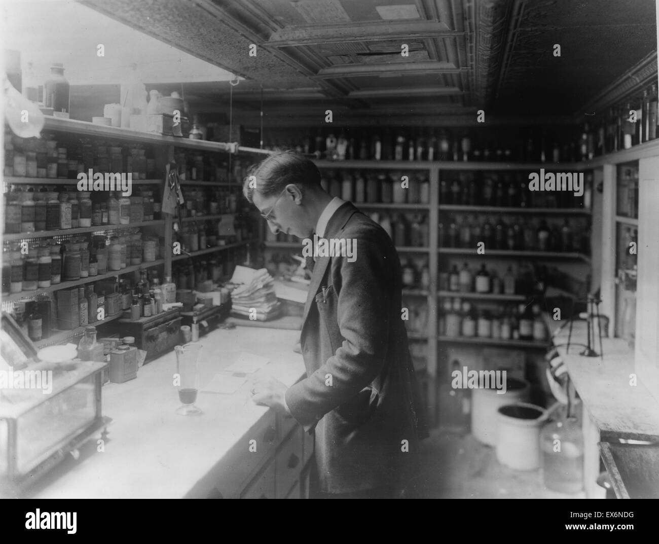 Pharmacist at People's Drug Store, 8th and H Streets, N.E., Washington, D.C., looking at prescriptions on the counter, in room lined with shelves of pharmacy bottles 1920 Stock Photo