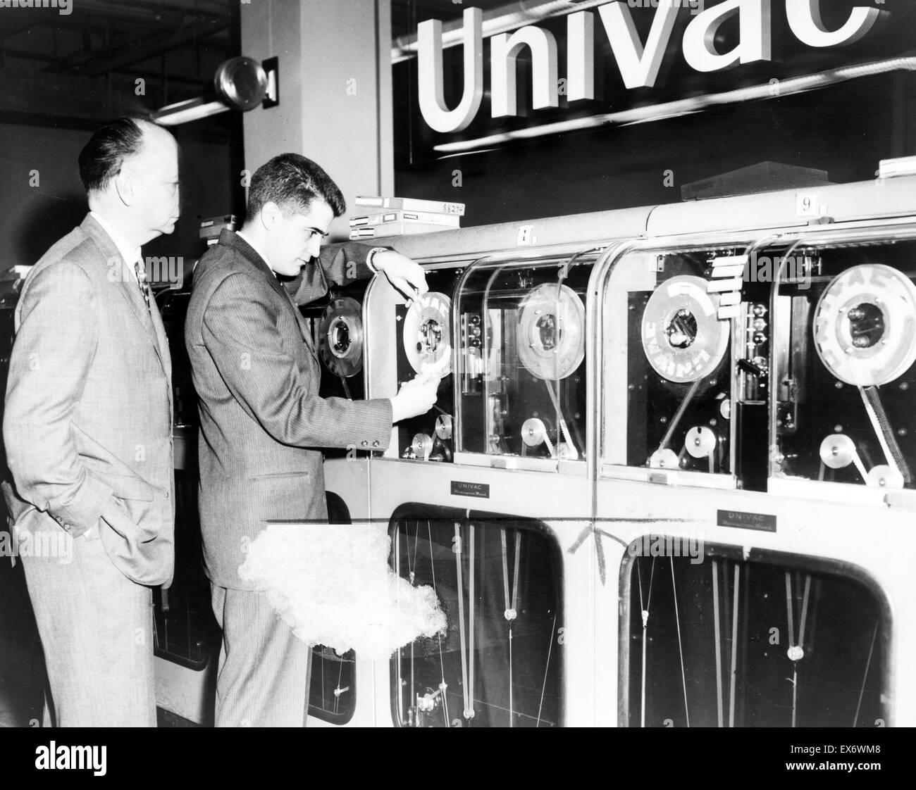 One man looks on as another man prepares Univac computer to predict a winning horse in a race Stock Photo