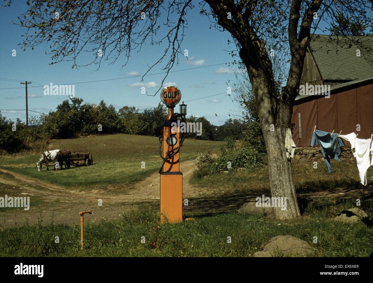 Gas pump with clothesline, barn and horse-drawn wagon in background. between 1941 and 1942. Colour. Stock Photo