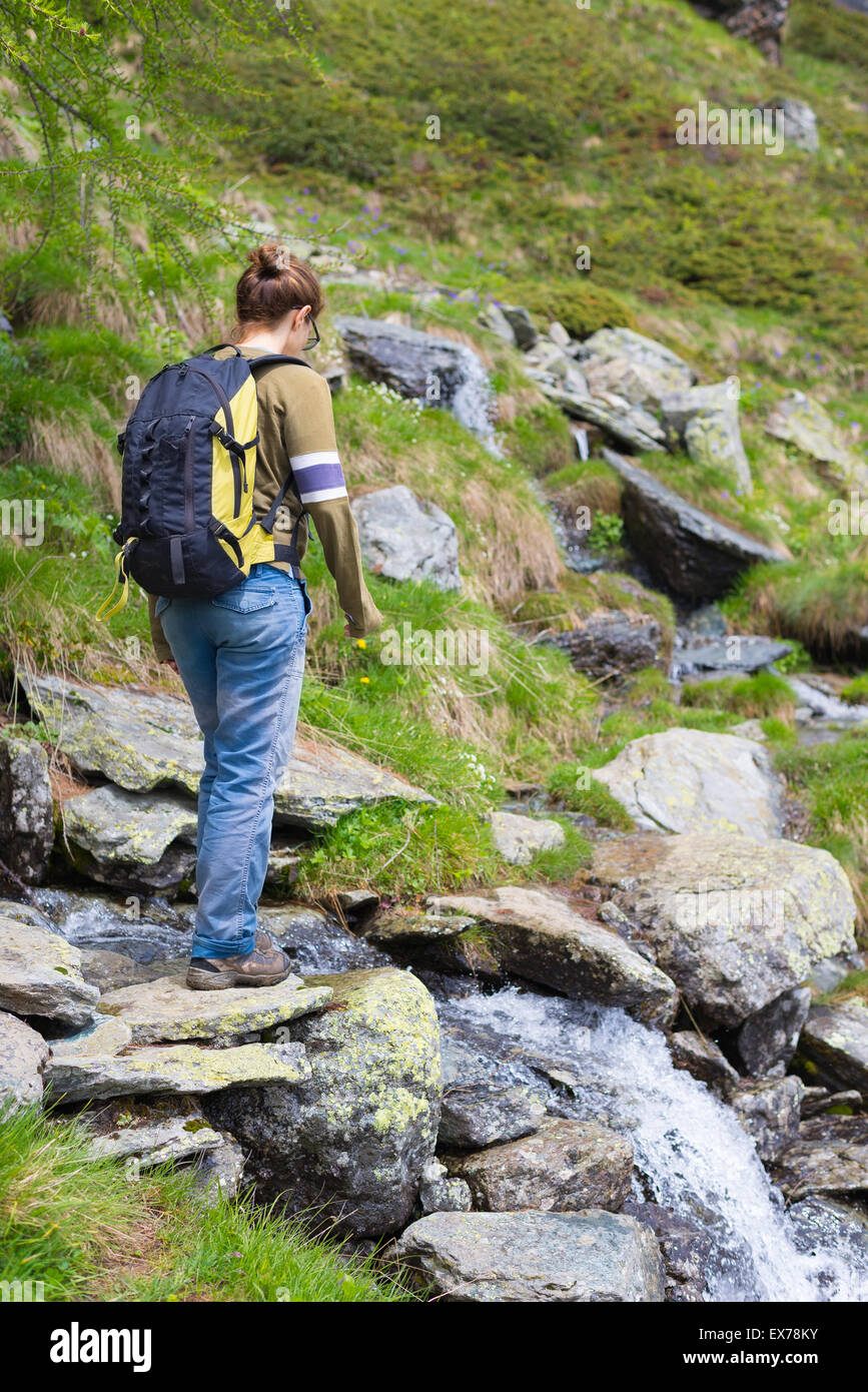 Female hiker with backpack crossing little stream in the mountains ...