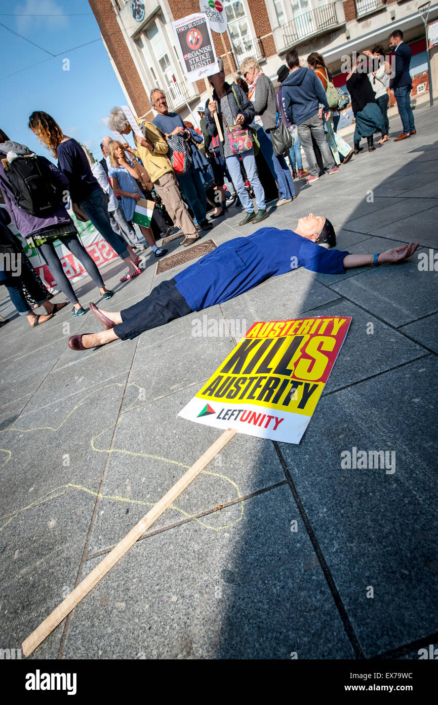 Exeter, Devon, UK. 8th July, 2015. A woman plays dead beside a Austerity Kills placard during the Exeter Budget Day Action #AusterityKills in Exeter City Centre on july 8th, 2015 in Bedford Square, Exeter, UK Credit:  Clive Chilvers/Alamy Live News Stock Photo