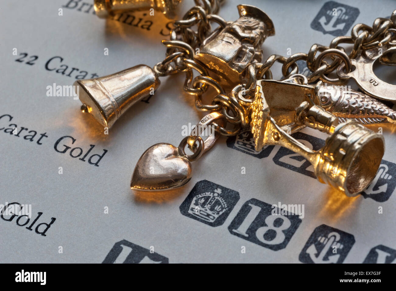 1960's gold charm bracelet and page of gold purity hallmarks reference book for scrap value evaluation Stock Photo