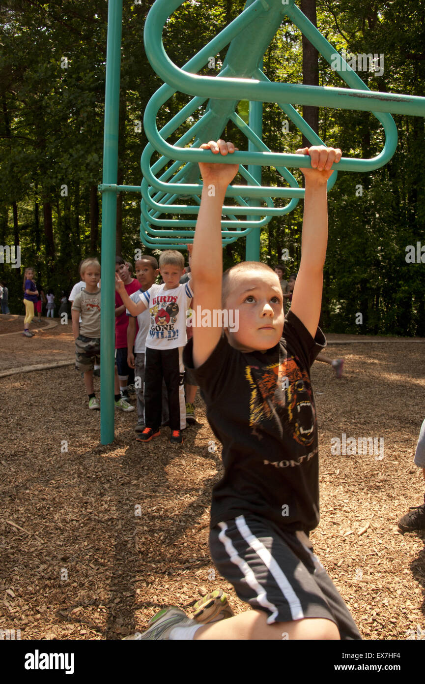 Child playing on a overhead ladder swing in a school playground Stock