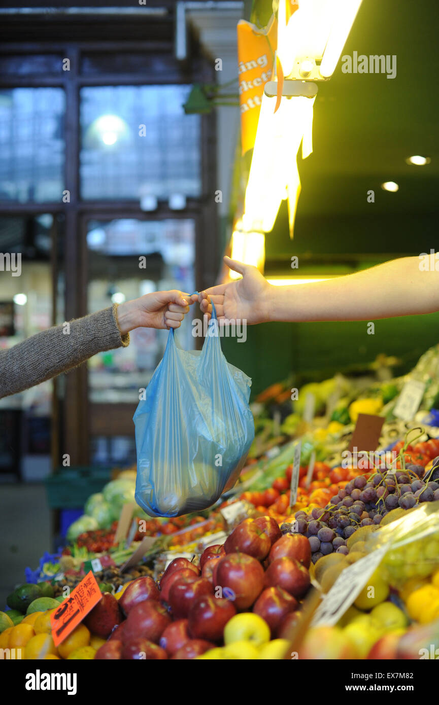 A woman hands over a bag of fruit and veg at a market stall. Stock Photo
