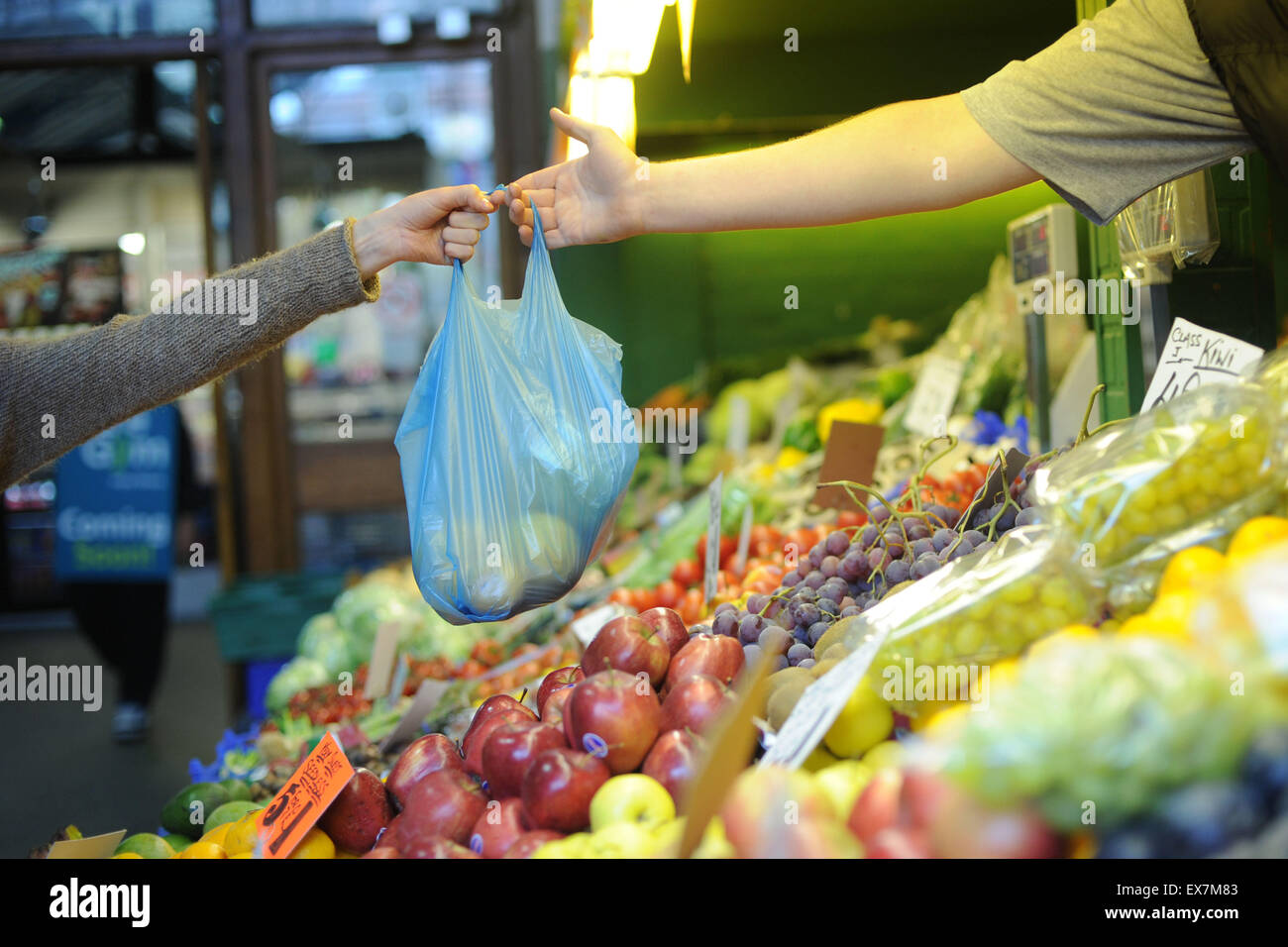 A woman hands over a bag of fruit and veg at a market stall. Stock Photo