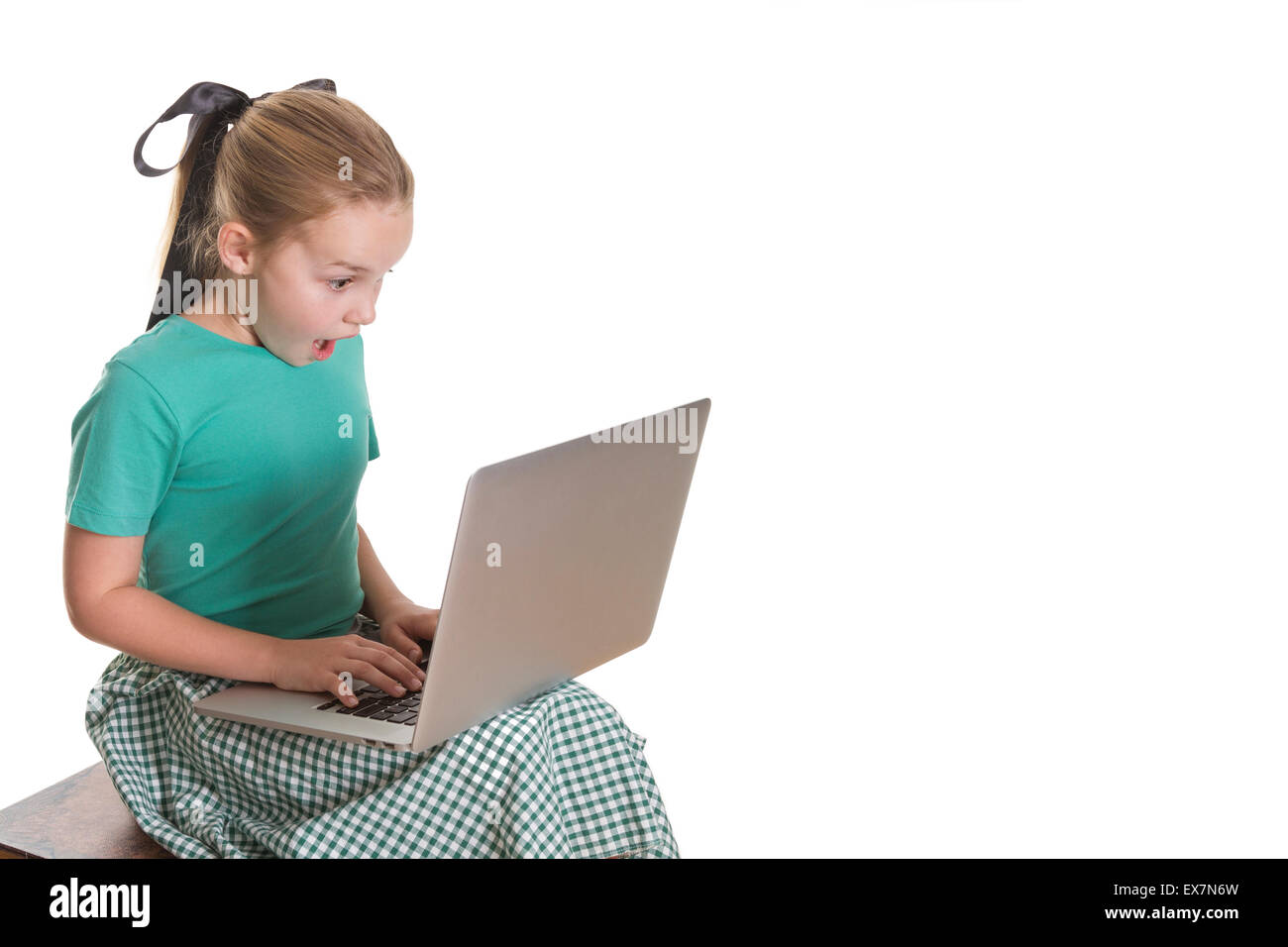 Young girl with a computer on her lap, looking shocked and amazed. Stock Photo