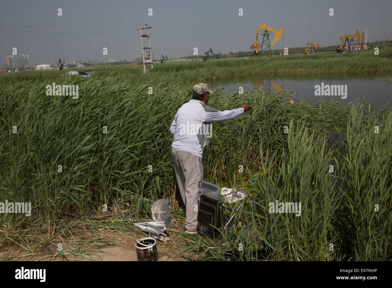 Daqing, China's Heilongjiang Province. 7th July, 2015. A man fishes near oil pumps in Daqing, northeast China's Heilongjiang Province, July 7, 2015. Daqing oilfield was discovered in 1959, which is the largest inland oilfield in China. On the 4,300 square kilometers oilfield, there are some 50,000 oil wells. © Jin Liwang/Xinhua/Alamy Live News Stock Photo