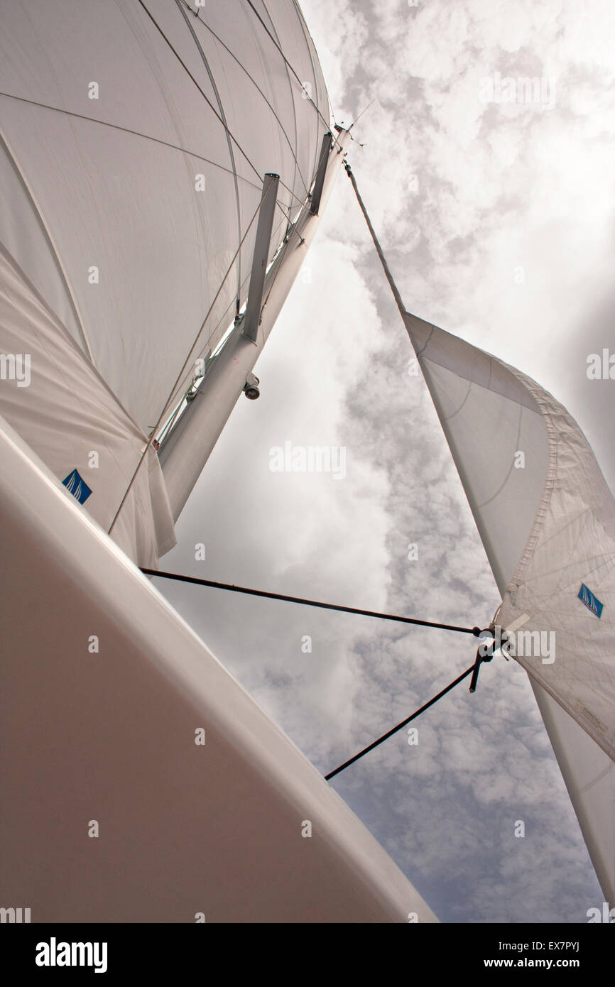 The sails of a luxury catamaran reach towards the sky and clouds Stock Photo