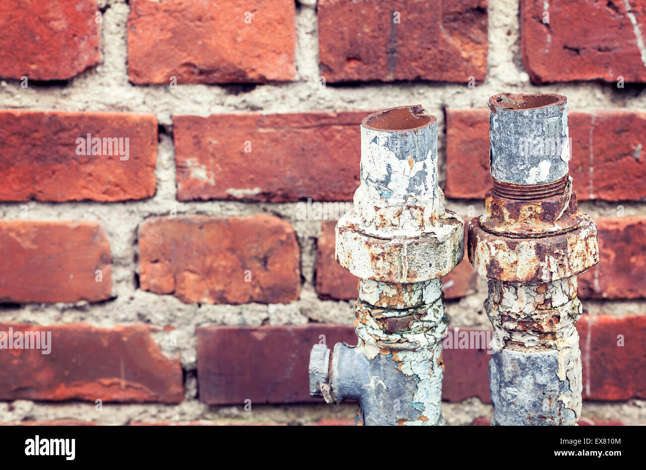 Old rusty cut pipes on a brick wall background. Stock Photo