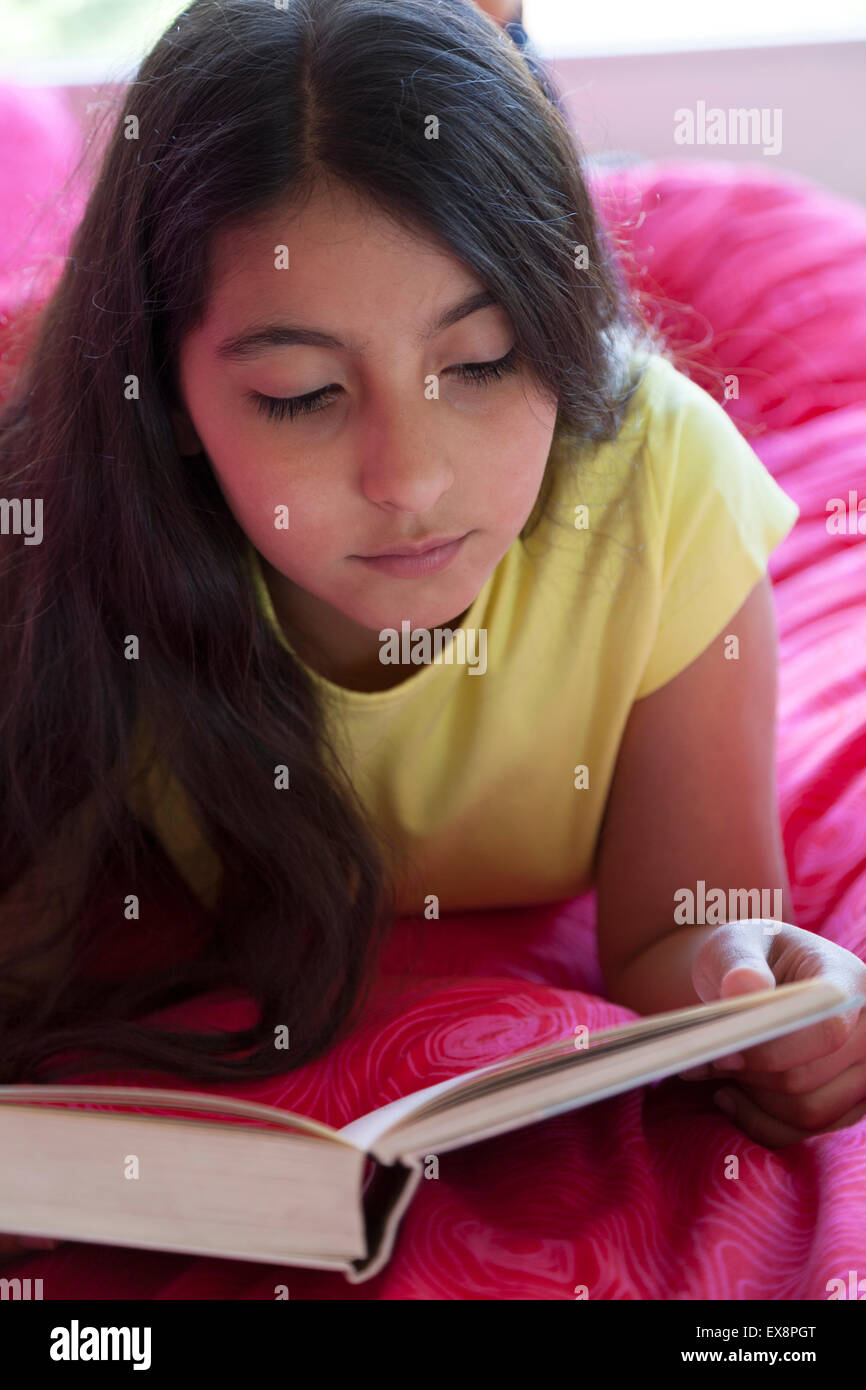 Teenage girl reading a book lying on her bed in her room Stock Photo