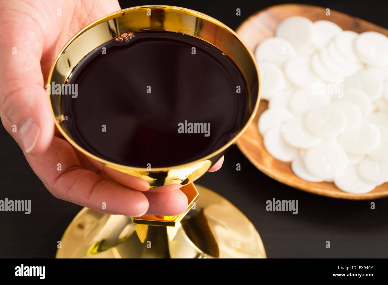 Christian holy communion, man's hand holding gold chalice with wine, communion wafer on plate Stock Photo