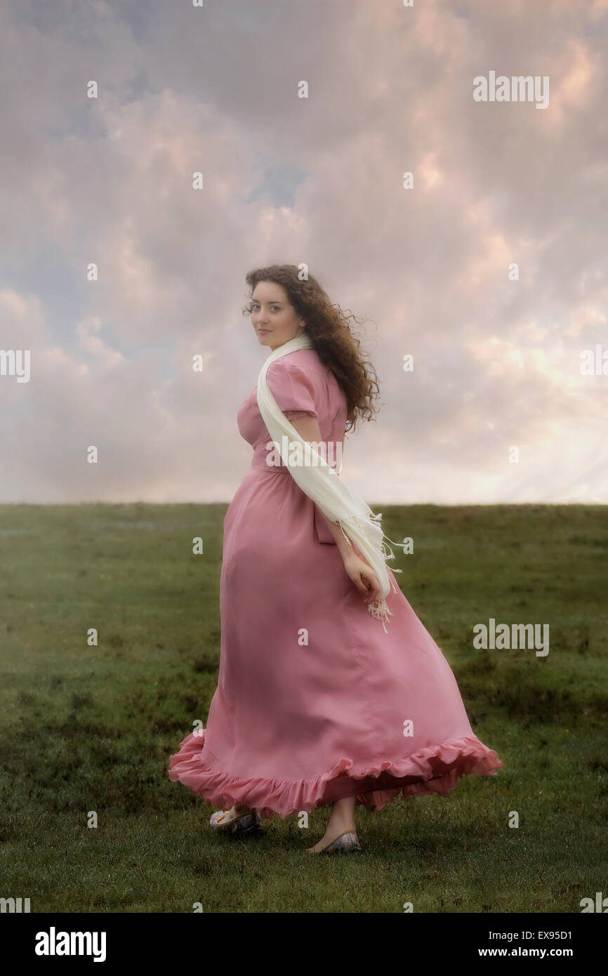 a woman in a pink dress is walking up a hill Stock Photo