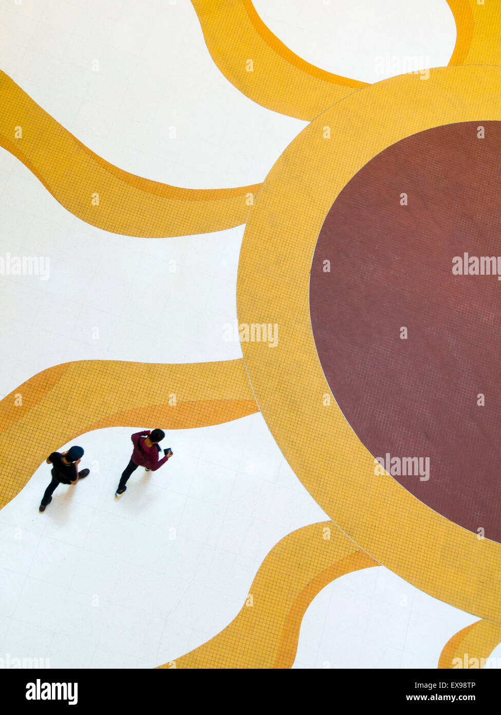 Two people walking towards a giant modern graphics of the sun on a white floor Stock Photo
