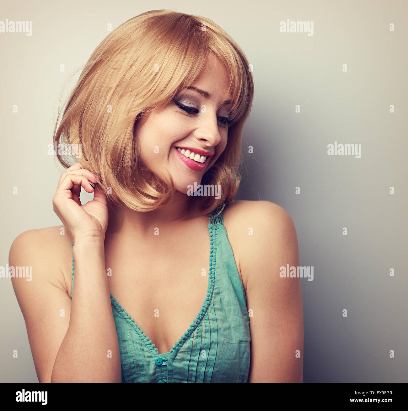 Pretty blond young woman with short hairstyle looking down. Natural smile. Color toned portrait Stock Photo