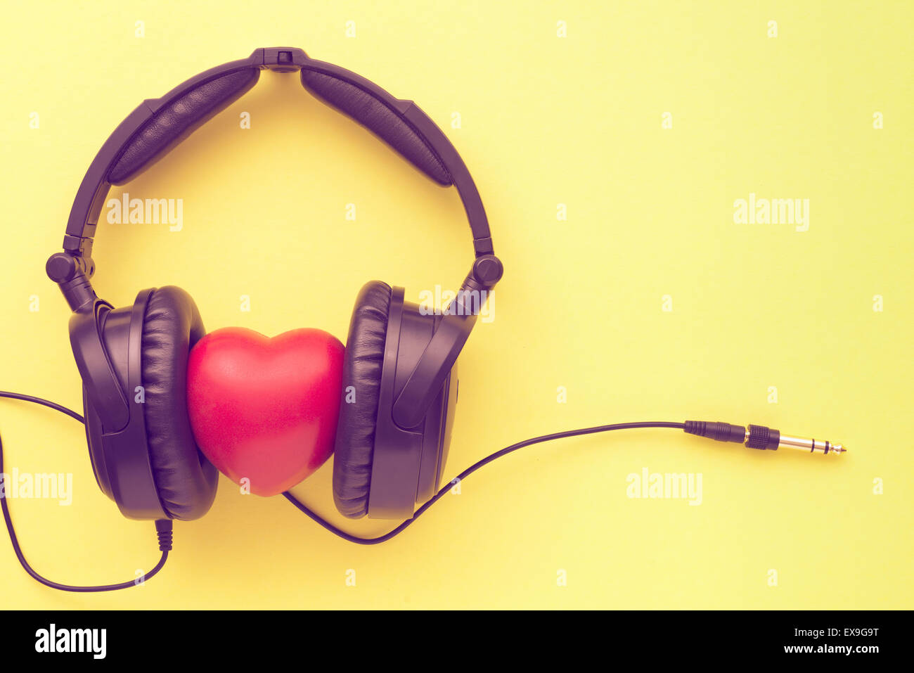 black headphones with red heart, wires and socket on yellow background Stock Photo