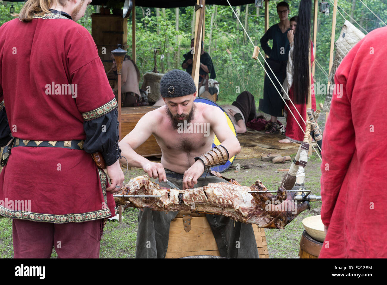 A man at a medieval festival carves a pig roast on a spit Stock Photo