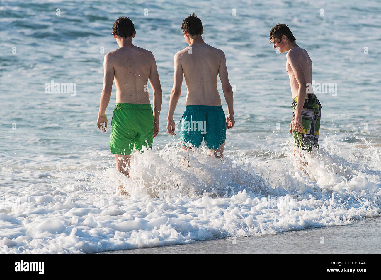 Three Teenagers standing in the surf on Fistral Beach in Newquay, Cornwall. Stock Photo