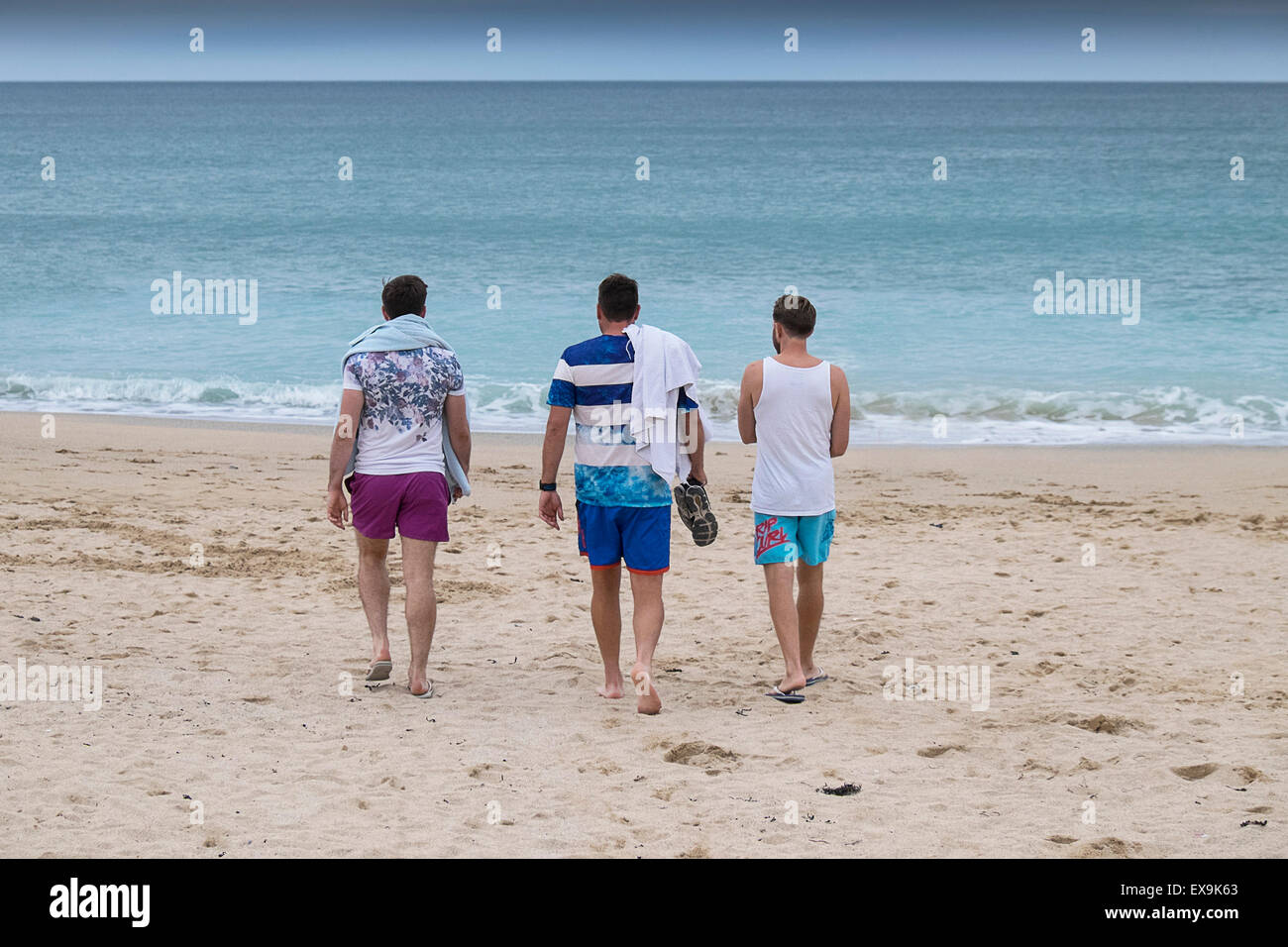Three holidaymakers walking down to the sea on Fistral beach in Newquay, Cornwall. Stock Photo