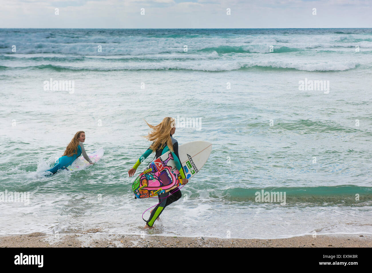 Two female surfers run into the sea at Fistral beach in Newquay