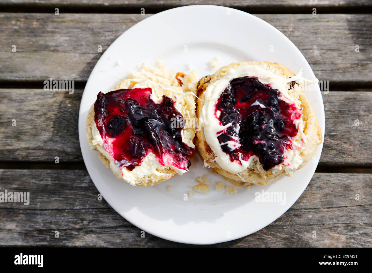 A traditional english Scone cut in half and spread with Cream and Jam. Part of a traditional English cream tea served outdoors Stock Photo