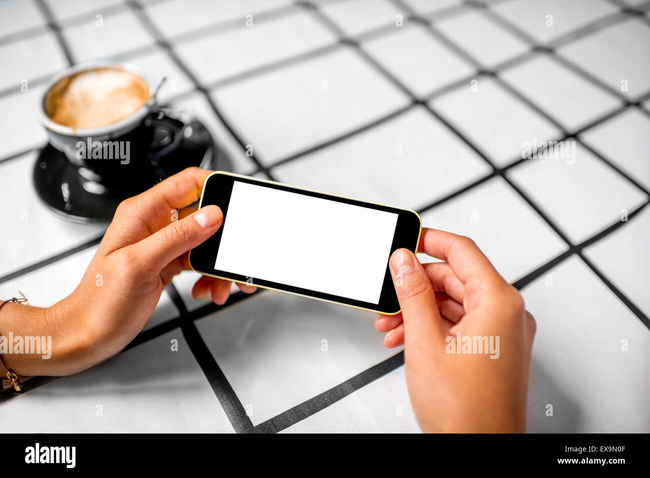 Female hand using a phone with isolated screen on checkered table with coffee cup. Stock Photo