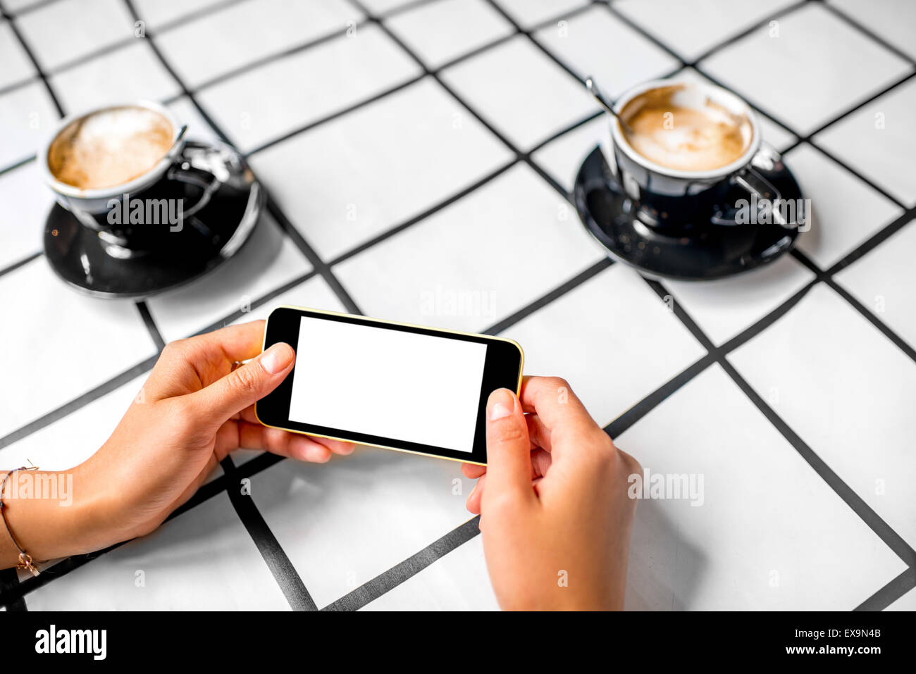 Female hand using a phone with isolated screen on checkered table with coffee cup. Stock Photo