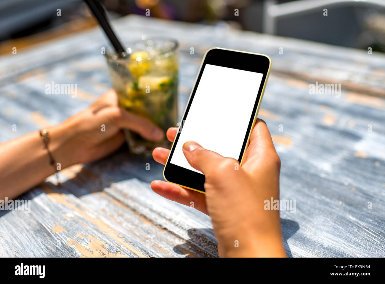 Female hand using a phone with isolated screen on wooden vintage table holding a glass with mohito Stock Photo