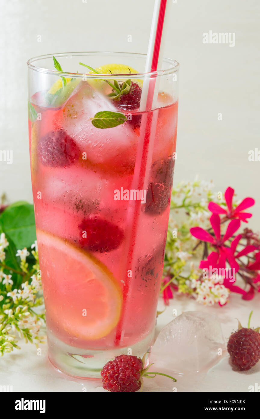 Homemade raspberry ice tea with lemon raspberry and ice cubes on a table decorated with flowers Stock Photo