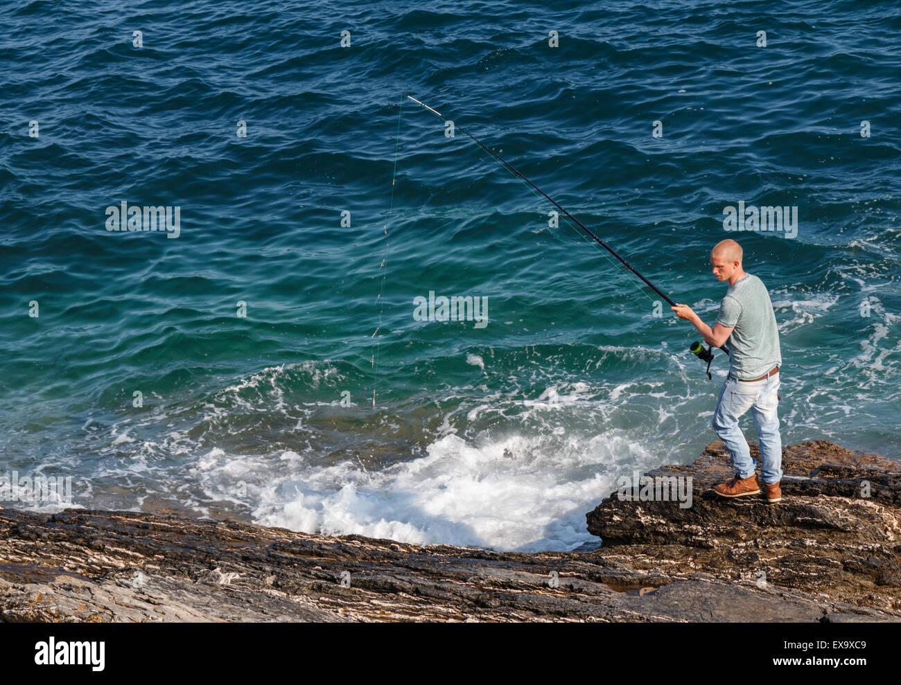 A male fisherman casting with a fishing rod from rocks into the sea Stock  Photo - Alamy