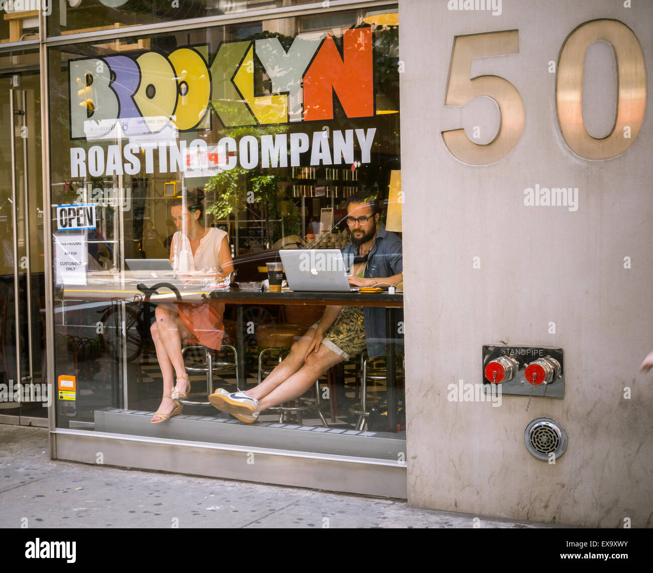 Customers with their laptop computers in the window of the Brooklyn Roasting Company in the Chelsea neighborhood of New York on Tuesday, July 7, 2015. (© Richard B. Levine) Stock Photo