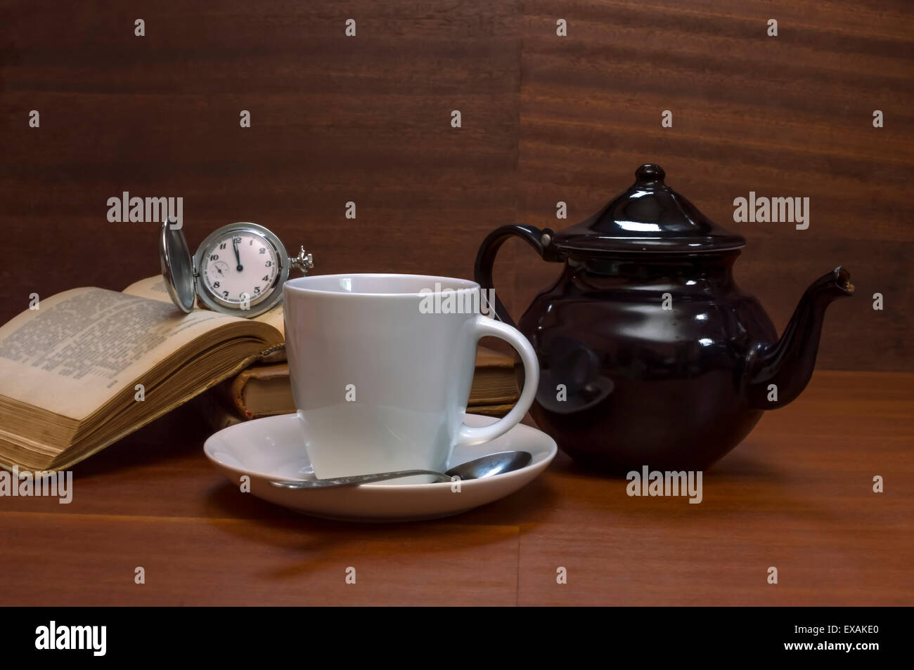 Tea cups with teapot, books and old pocket watch on wooden table