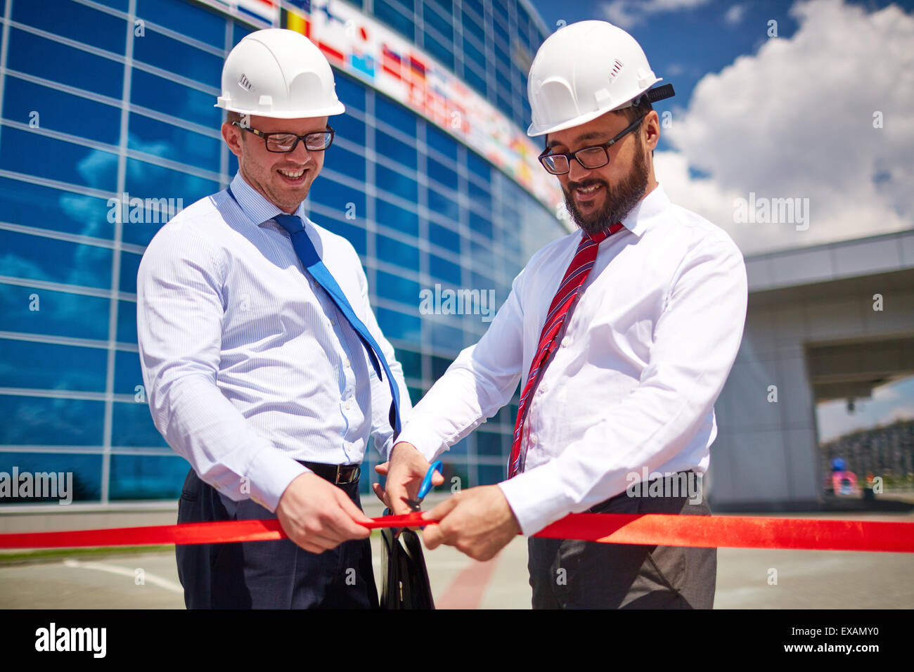 Happy architect cutting red ribbon at official opening of new construction Stock Photo