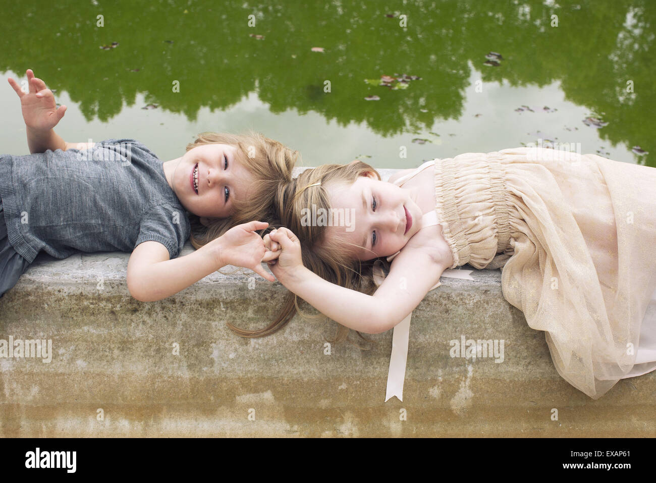 Young sisters lying down on beside pond,holding hands Stock Photo