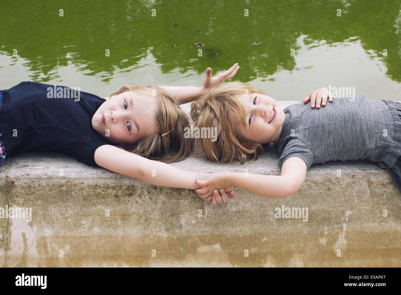 Little girls lying together beside pond, holding hands Stock Photo