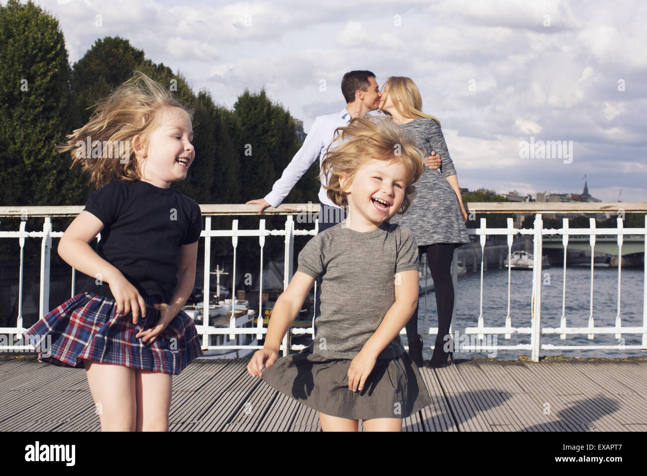 Little girls playing outdoors while their parents kiss in the background Stock Photo