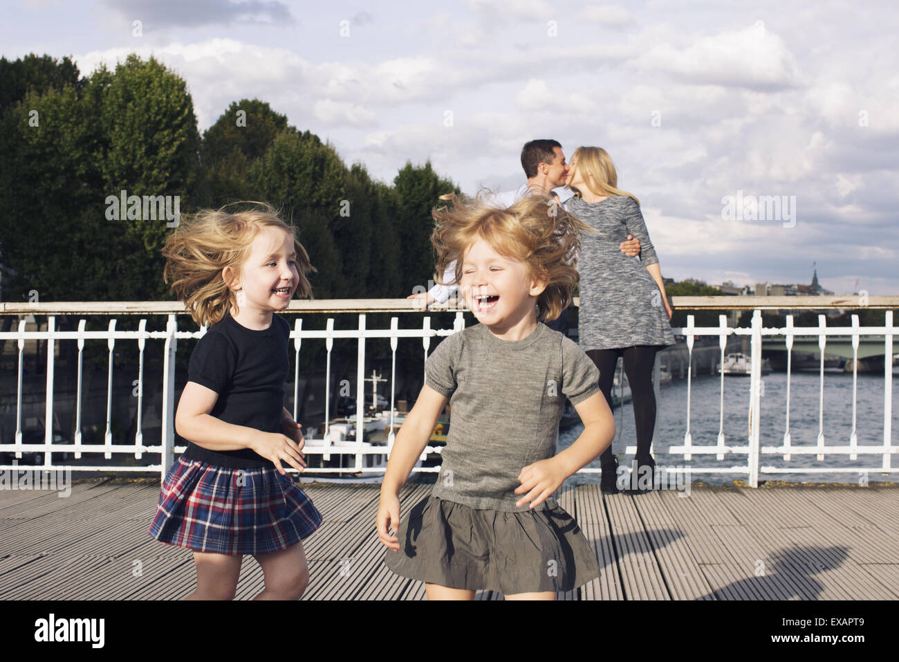 Little girls playing outdoors while their parents kiss in the background Stock Photo